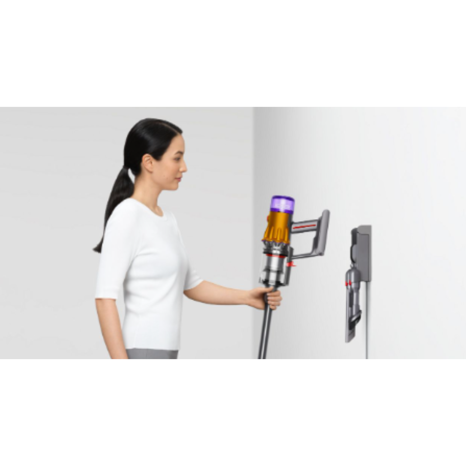 Woman hanging a Dyson cordless vacuum on a wall-mounted charger.