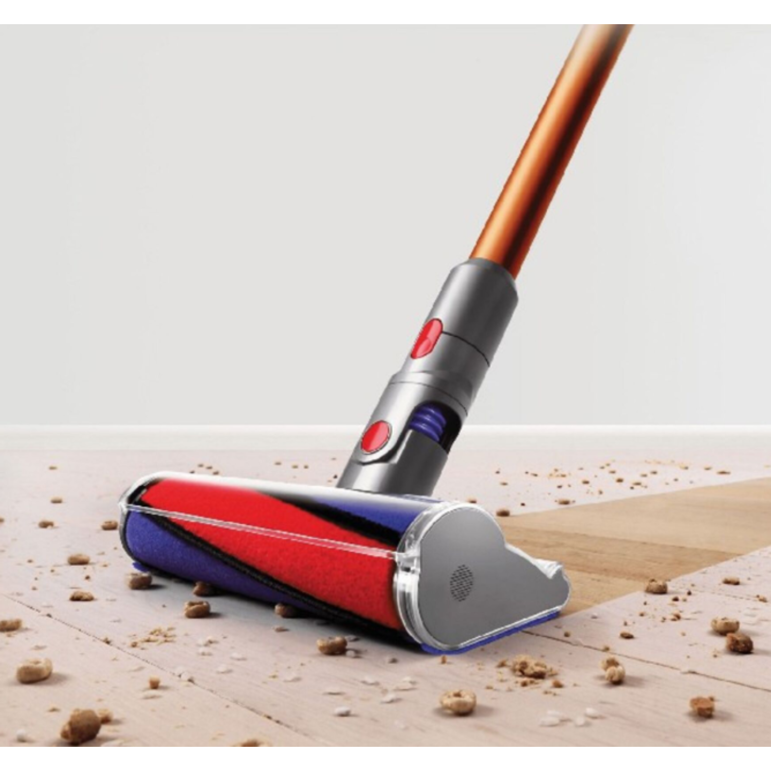 Dyson vacuum cleaner head on wooden floor with debris.