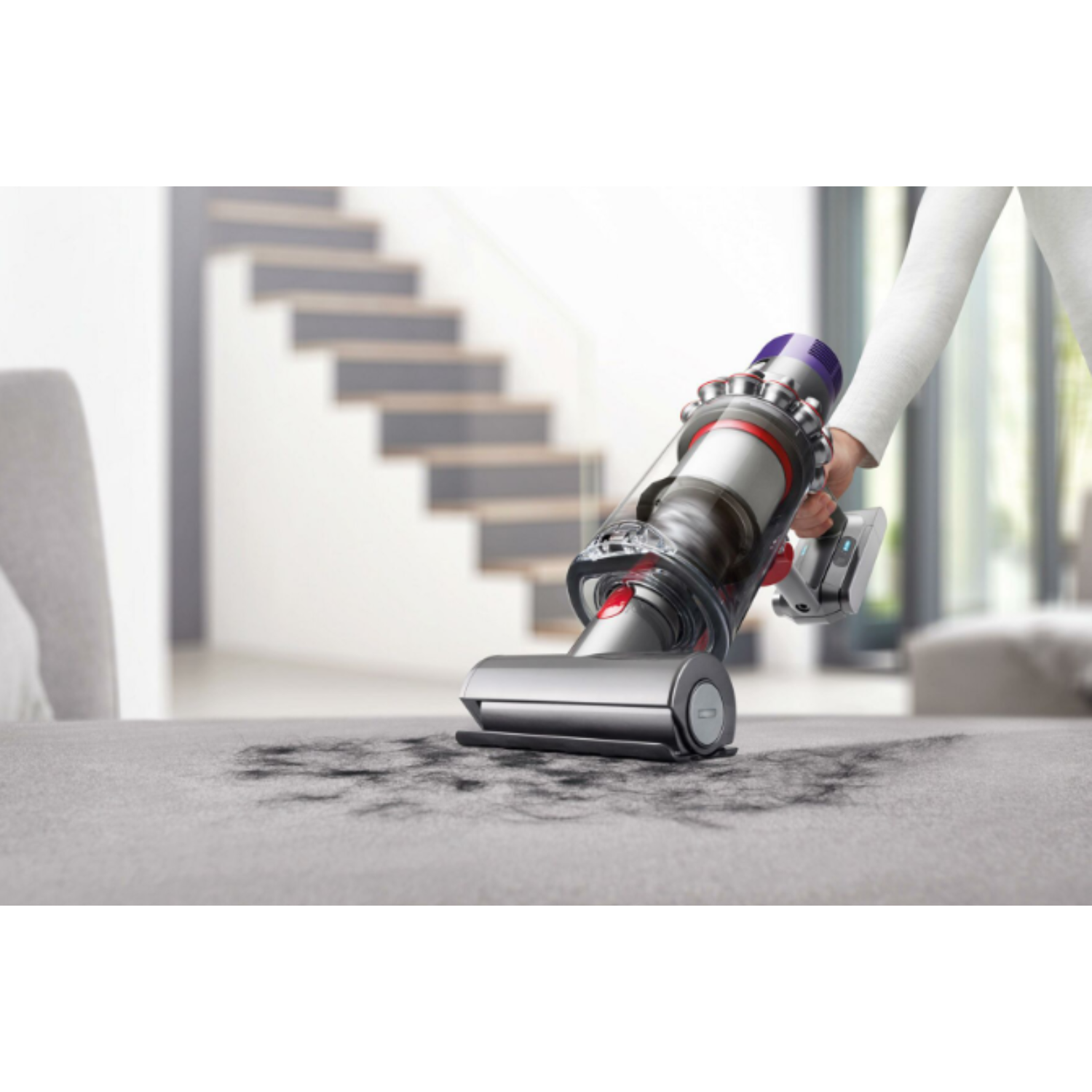 Person vacuuming a carpet with a cordless vacuum cleaner in a modern living room.