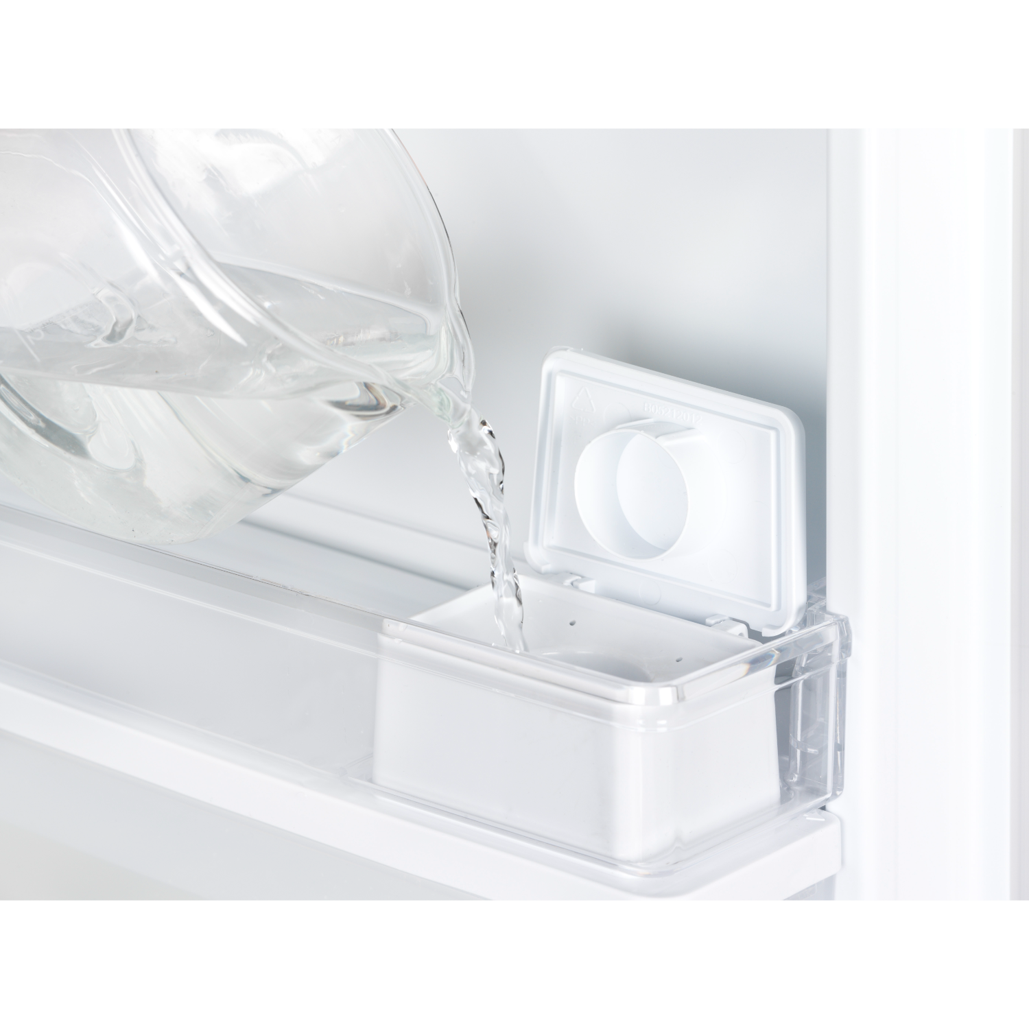 Water being poured into a white container inside a refrigerator.