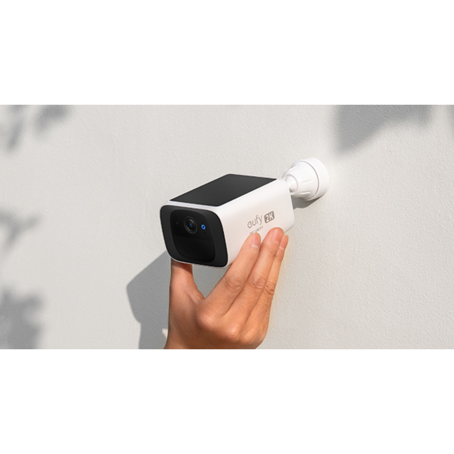 La main d'une personne monte une caméra de sécurité blanche et noire sur un mur blanc.