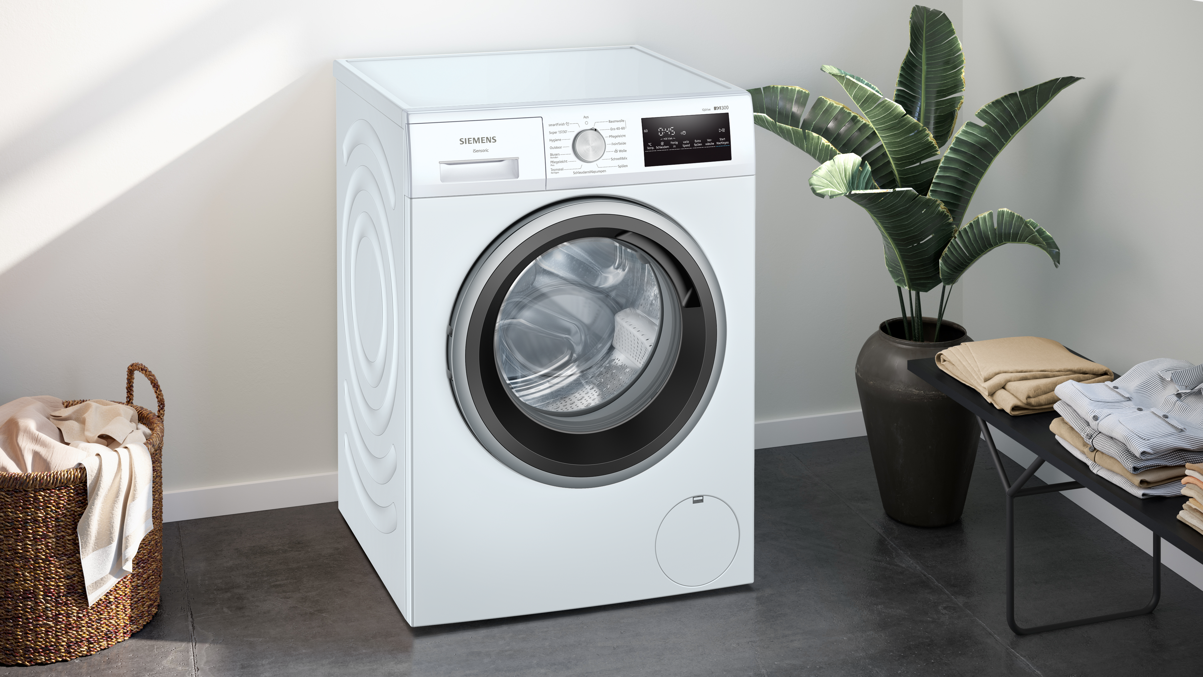 Weiße Siemens Waschmaschine, Seitenansicht, neben einer Pflanze und einem Korb. Weißer Hintergrund.