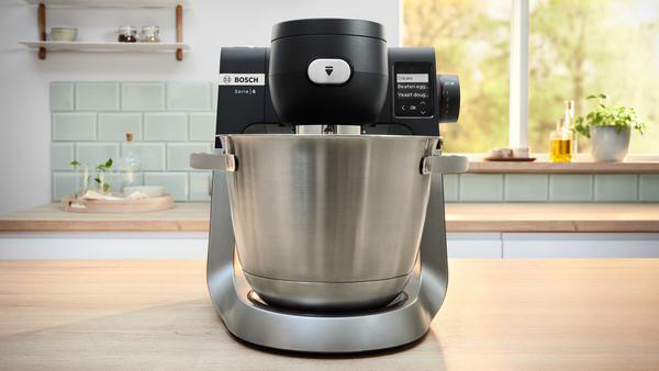Ein silberner Bosch Serie 6 Food Processor mit Edelstahl-Schüssel, auf einer Holz-Arbeitsplatte.