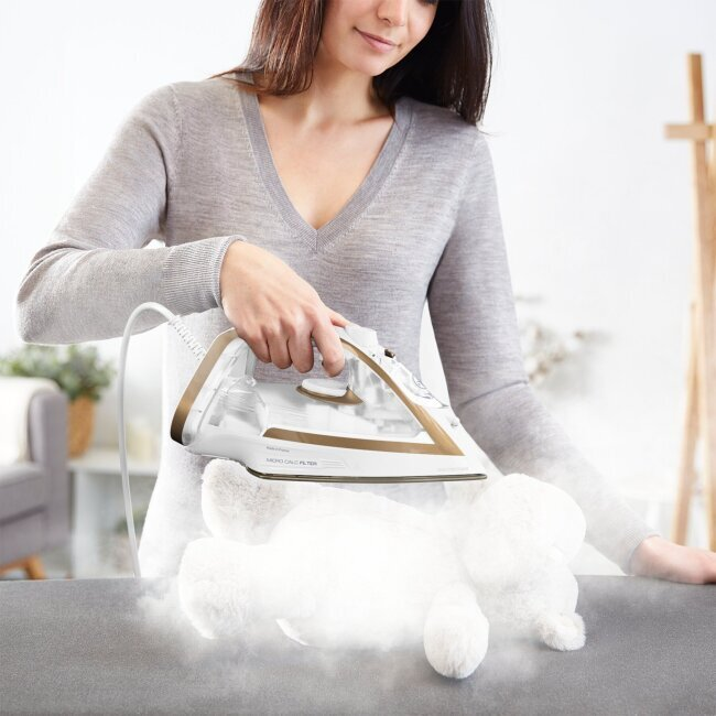 Ręka kobiety używająca żelazka parowego na tkaninie.