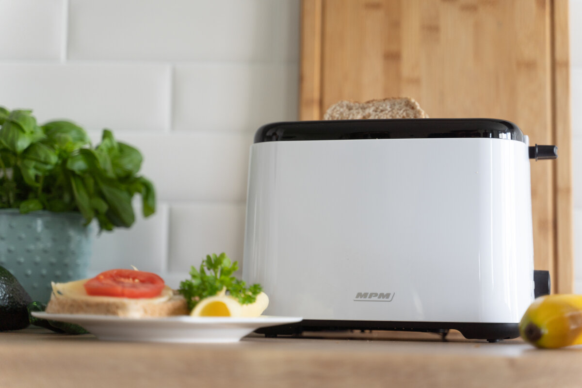 Biały toster z wyskakującą kromką chleba i talerzem z jedzeniem.