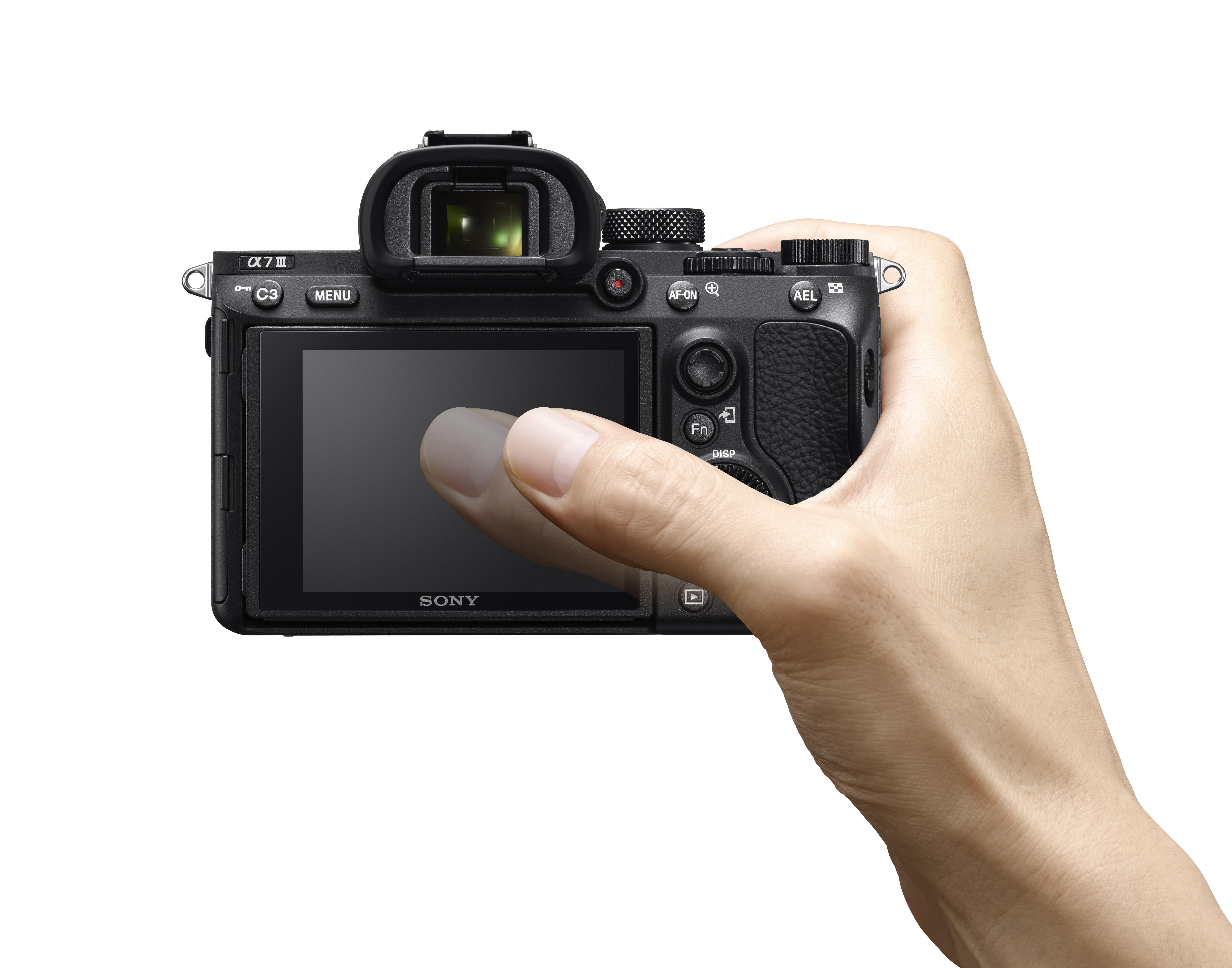 Eine Hand, die eine schwarze Sony Alpha 7 III Kamera hält und ihren Bildschirm berührt.