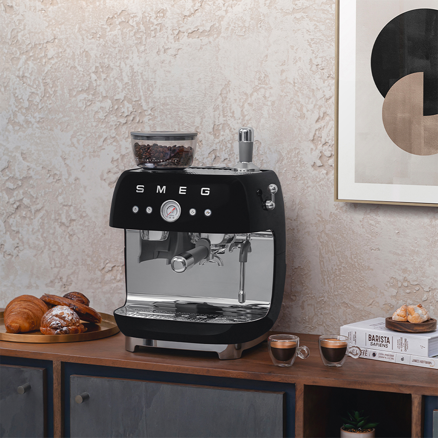 Macchina da caffè espresso nera con contenitore chicchi, due tazzine e pasticcini su vassoio.