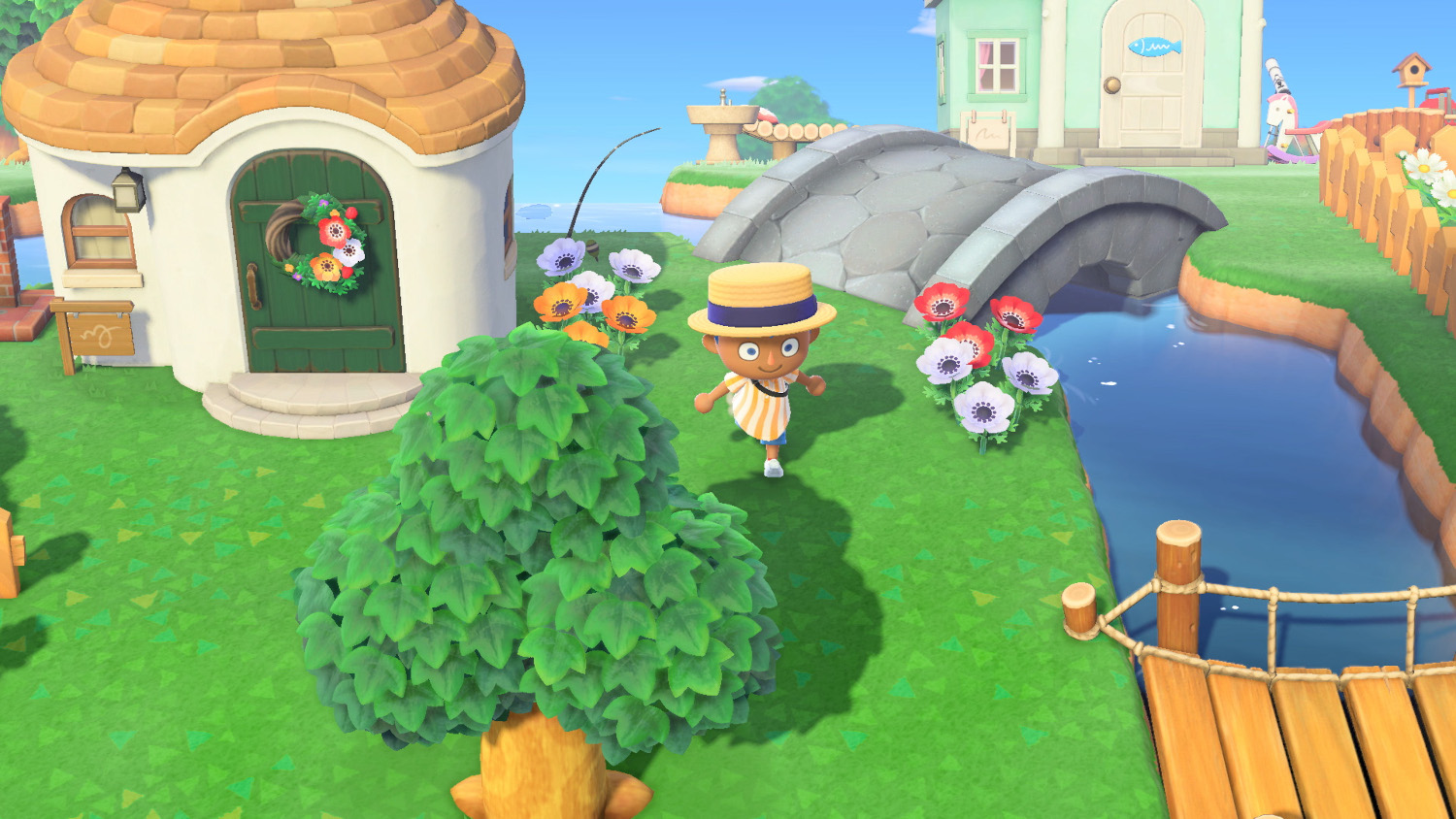 Une personne en vêtements rayés marche sur un sentier dans un village de style cartoon. Fleurs et un pont sont à proximité.
