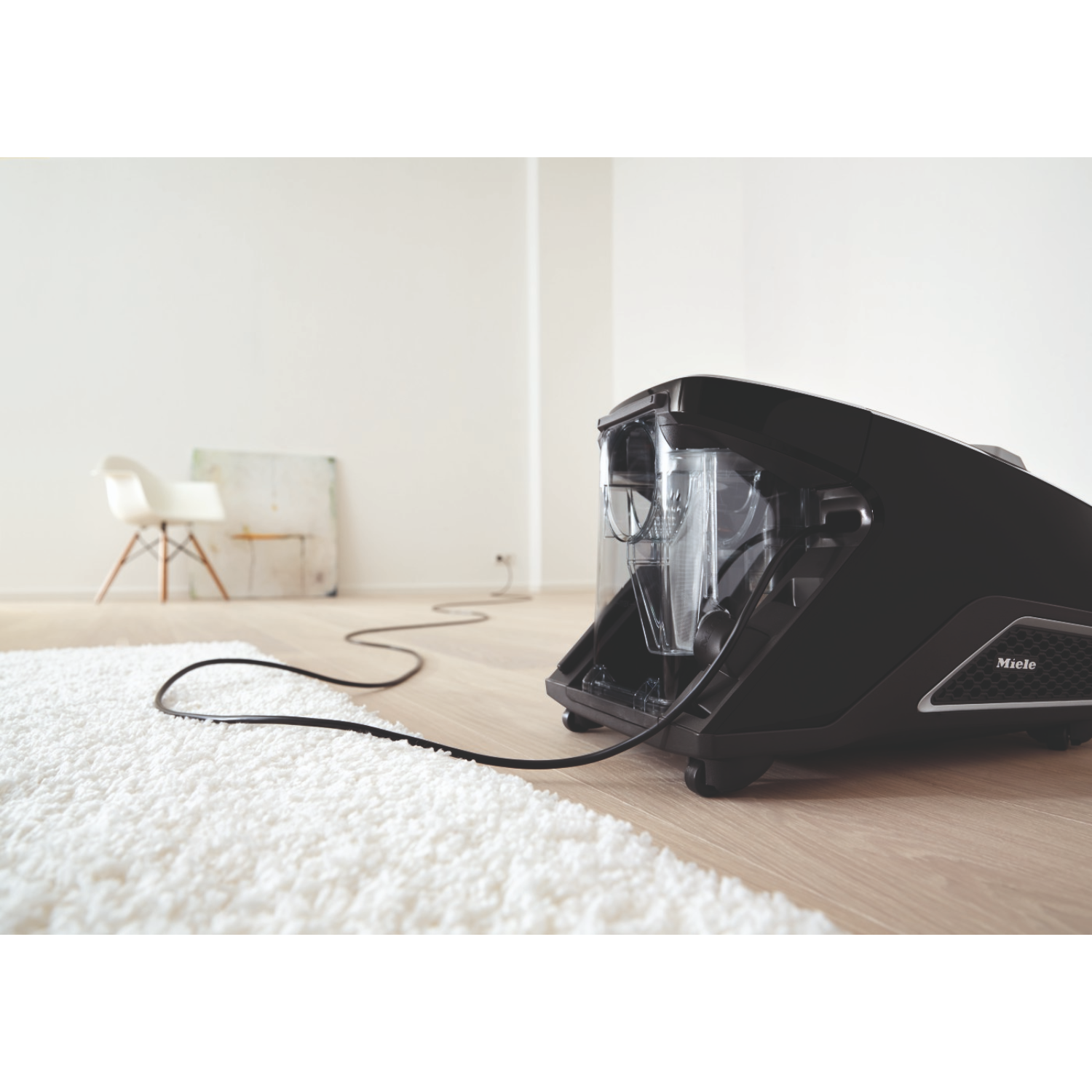 A black vacuum cleaner on a white carpet in a room with a white wall.