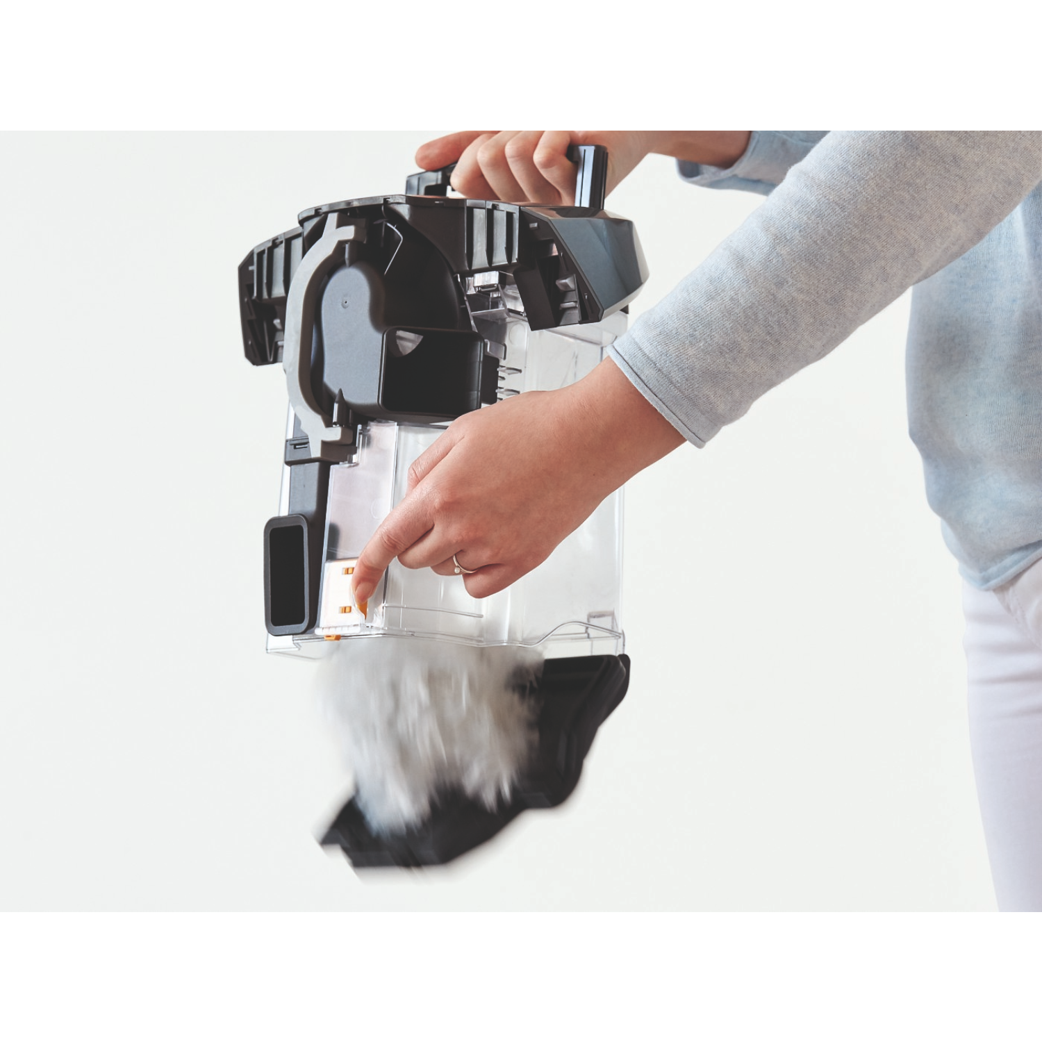A person's hands holding a vacuum cleaner dust container, emptying contents into a bag.