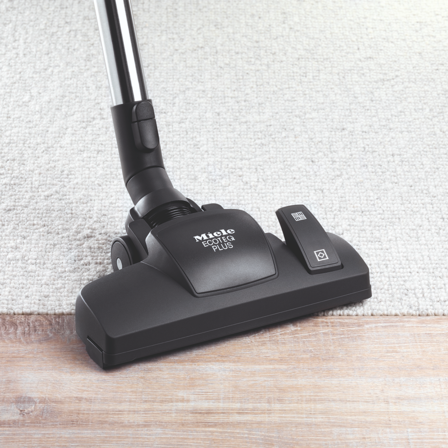 A vacuum cleaner nozzle on a light carpet, with the brand name Miele.