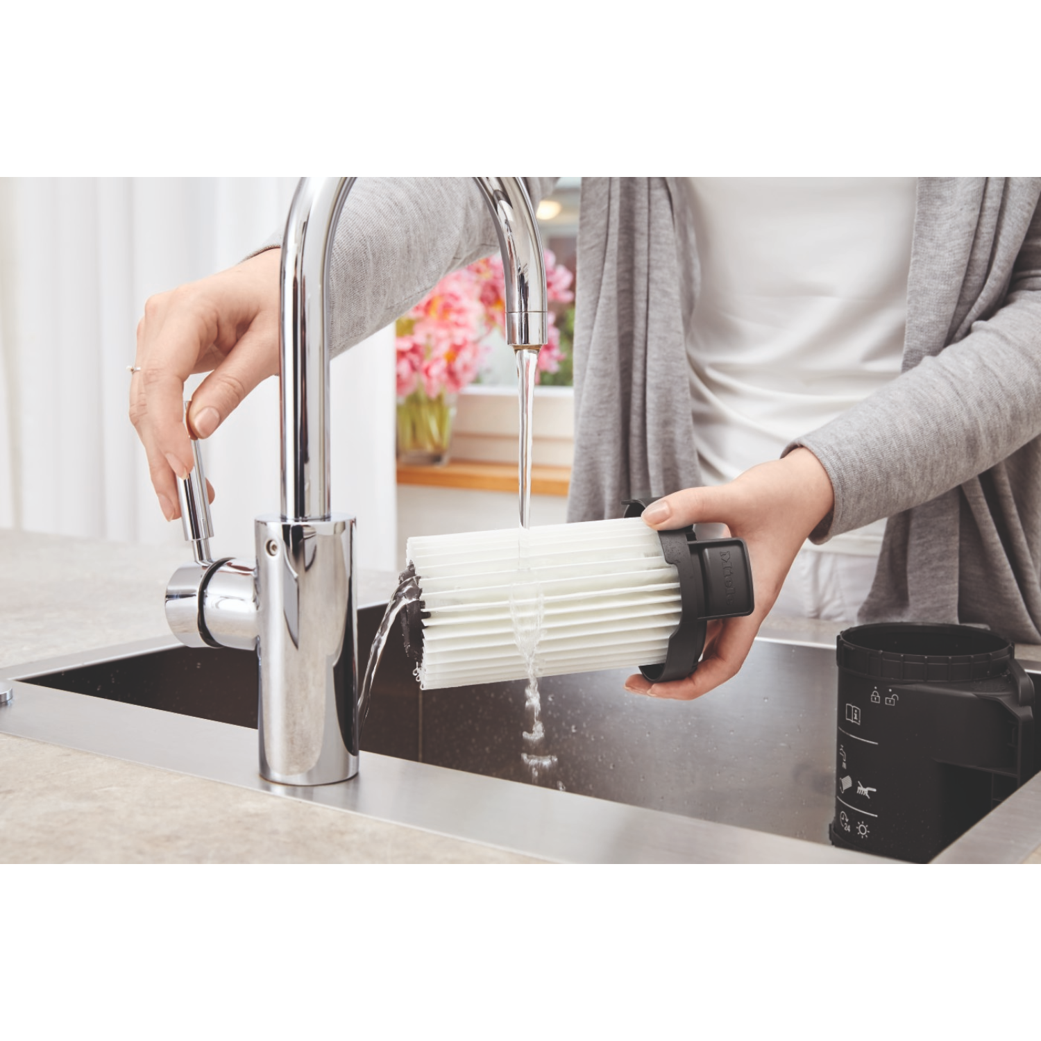 Person washing a filter under a faucet in a kitchen sink.