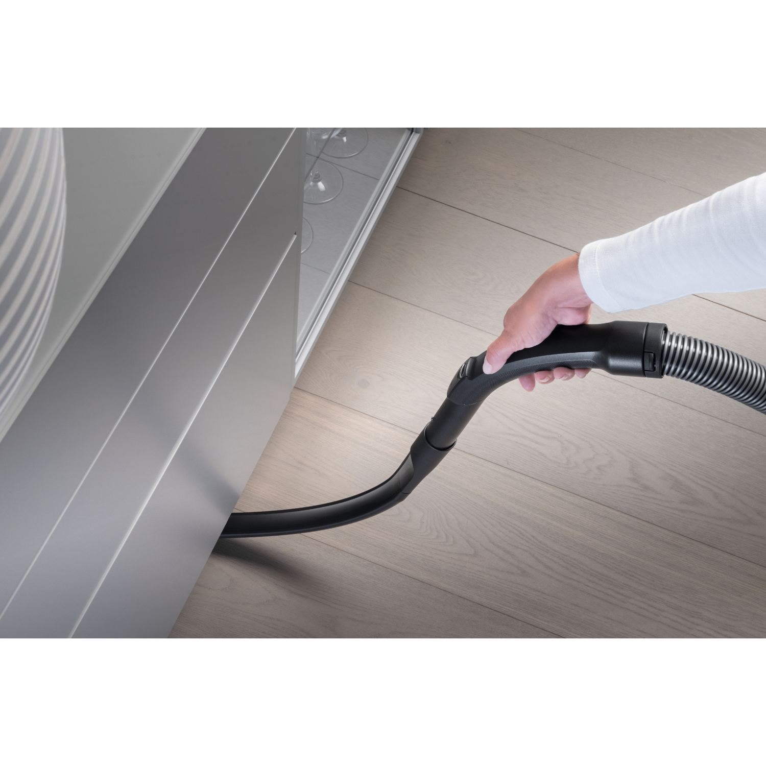 Hand vacuuming the floor near a cabinet. Shows the vacuum hose and floor.