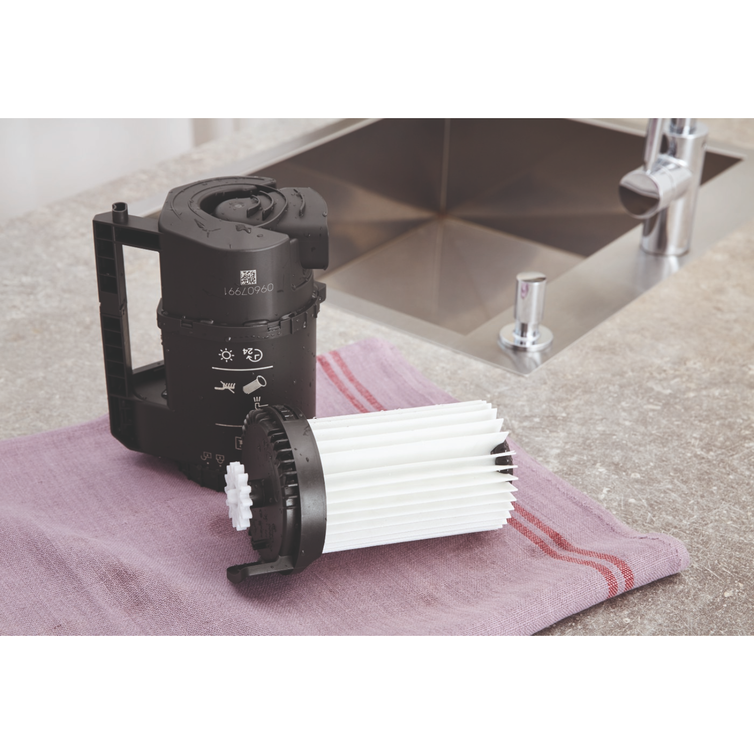 Black vacuum cleaner filter and its housing on a lavender cloth near a sink.