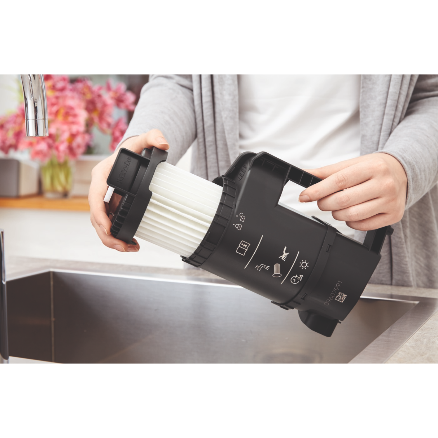 Person holding a vacuum filter over a stainless steel sink, with pink flowers in background.
