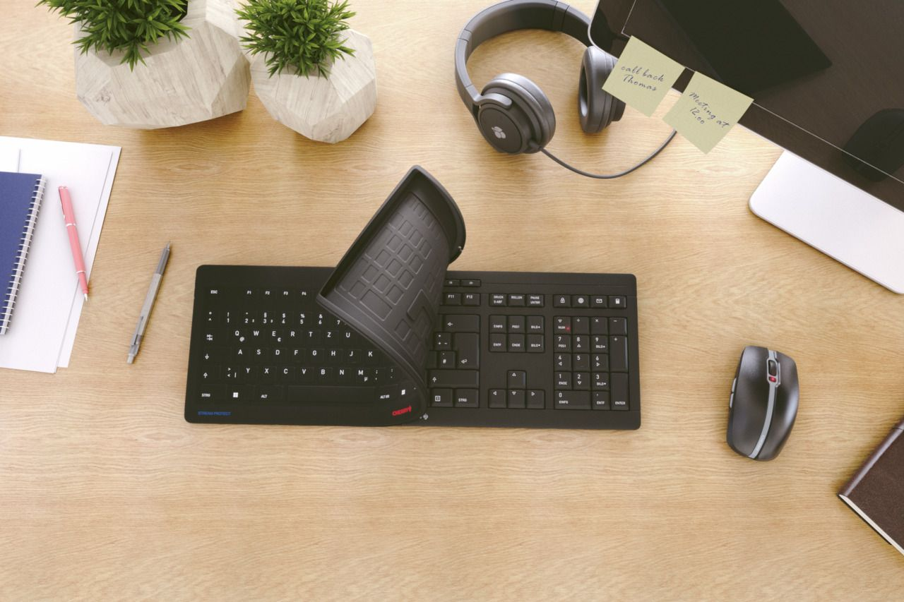 Schwarze Tastatur mit gebogener Gummiabdeckung und anderem Schreibtischzubehör.