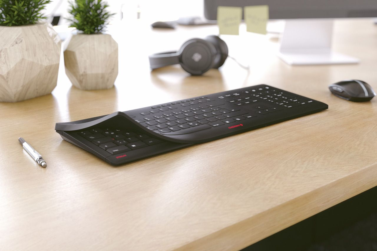 Schwarze, gebogene Tastatur auf einem Holztisch. Maus und Stift sind ebenfalls sichtbar.