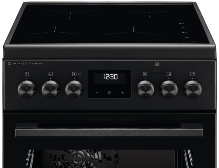 Czarny piekarnik z wyświetlaczem cyfrowym pokazującym godzinę 12:30. Widoczne pokrętła i elementy dotykowe.