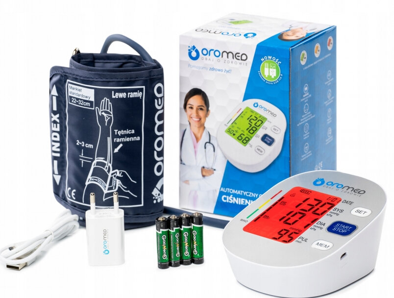 Ciśnieniomierz z mankietem, wyświetlaczem, ładowarką i bateriami. Zapakowany, z instrukcją. Białe tło.