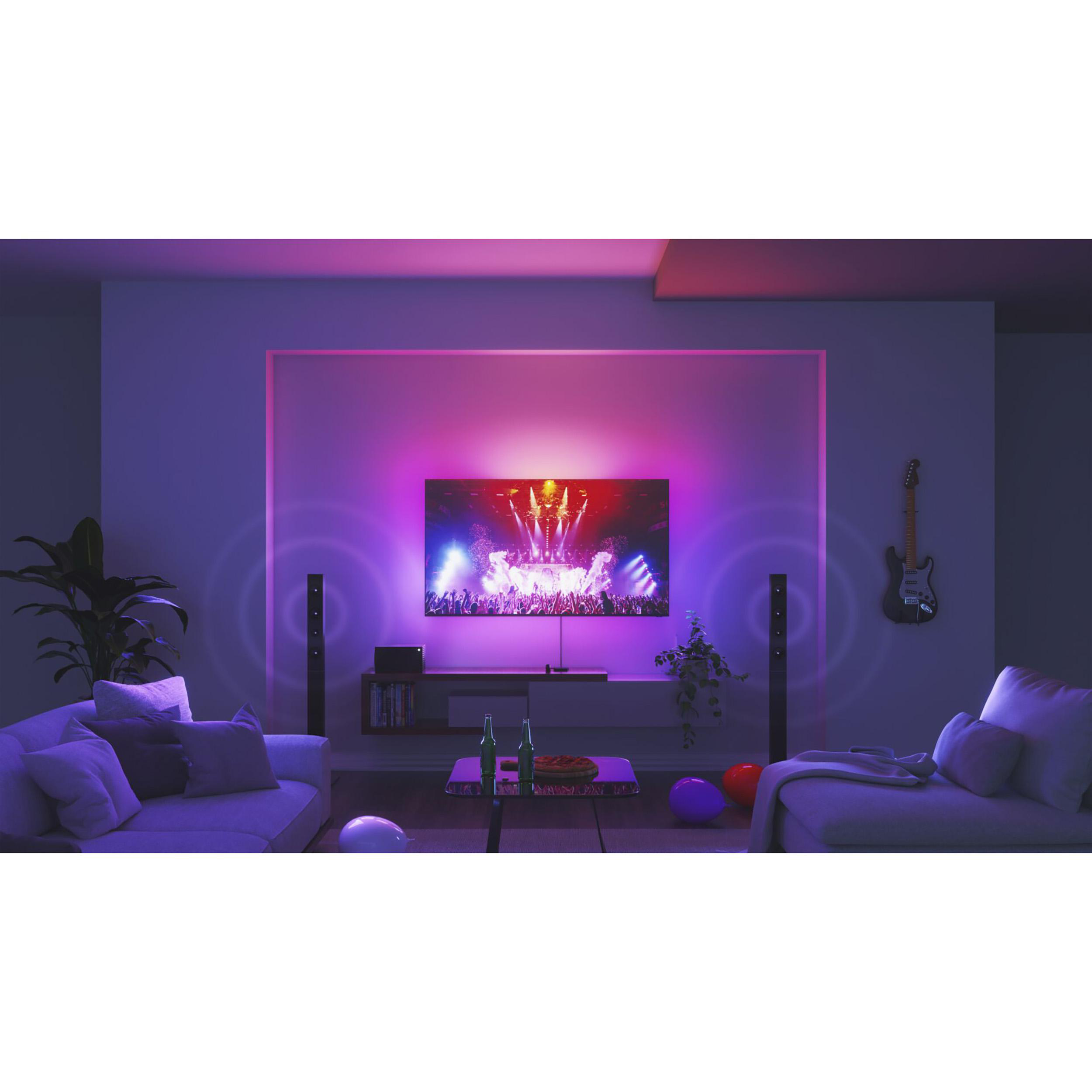 Wohnzimmer mit großem Fernseher, der eine Konzertszenen zeigt, flankiert von Lautsprechern. Lila und blaues Licht.