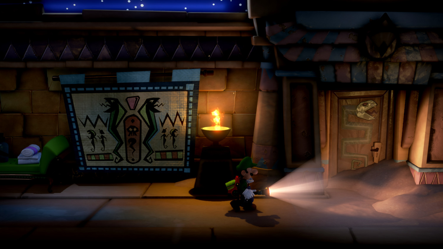 Nachtscène uit een videogame. Een personage met een zaklamp staat voor een gebouw.