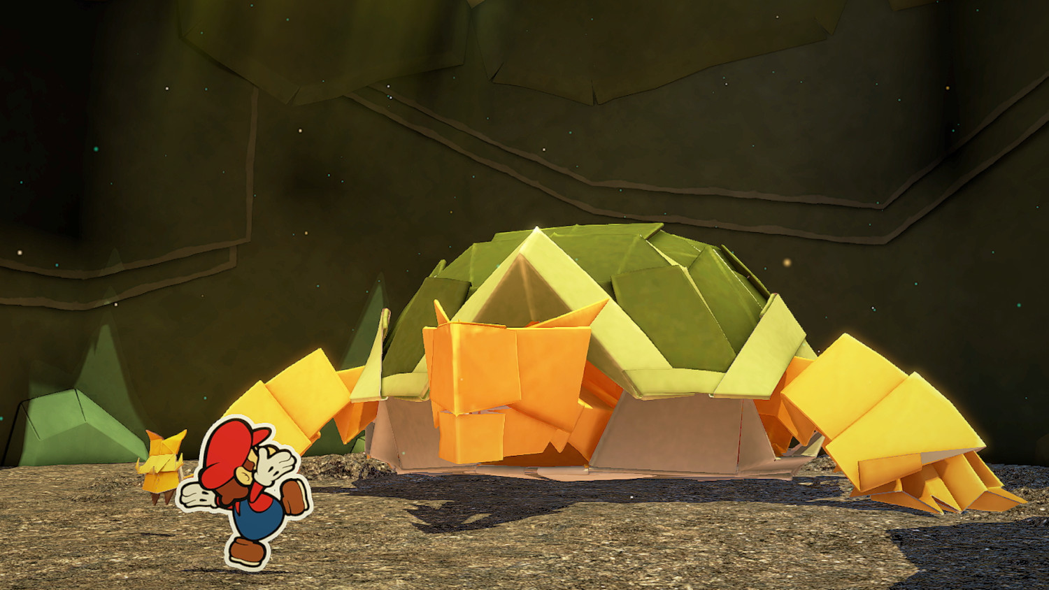 Mario fuit Bowser en papier dans une grotte. Bowser est grand, carapace verte et orange.