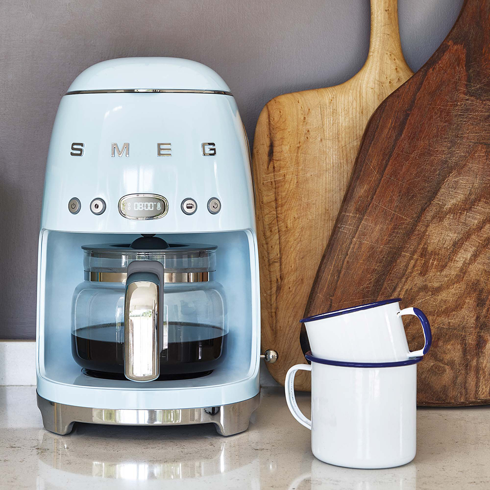 Macchina da caffè retrò azzurra con caraffa in vetro. Due tazze bianche con bordi blu.