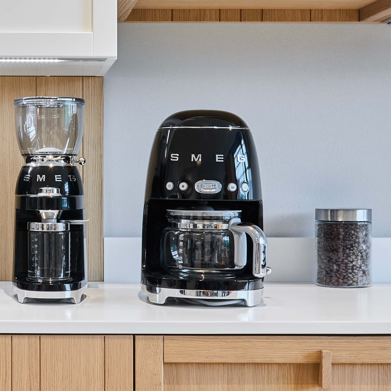 Caffettiera, macinacaffè e barattolo di chicchi di caffè SMEG neri su un bancone bianco.