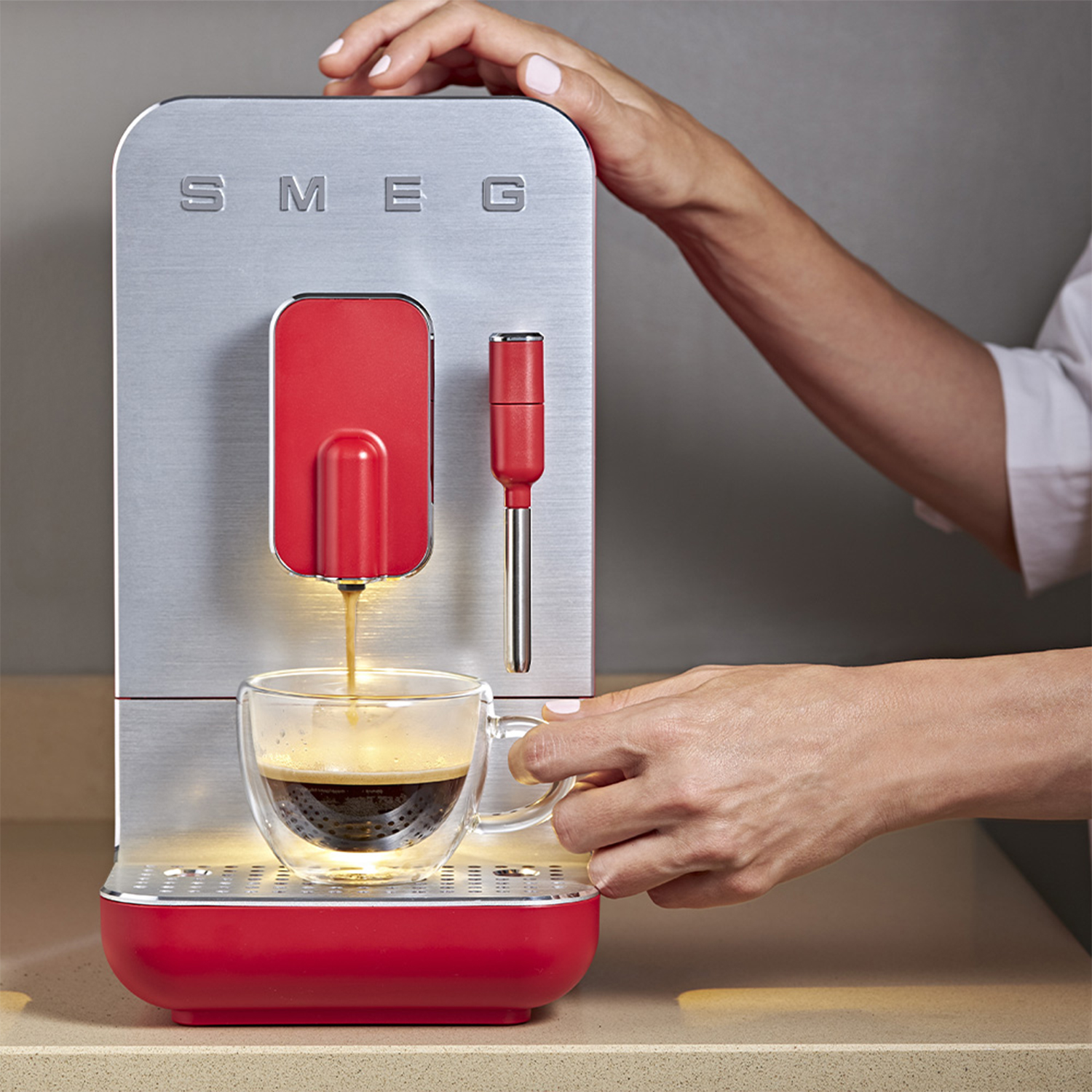 Macchina per espresso SMEG argento e rossa. Una persona versa il caffè in una tazza di vetro.