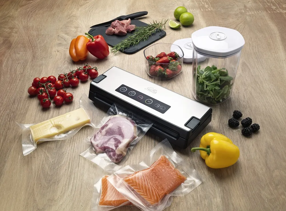 Vakuumiergerät mit Lebensmitteln: Gemüse, Fleisch, Käse, Erdbeeren, Brombeeren und Lachs. Holzoberfläche.