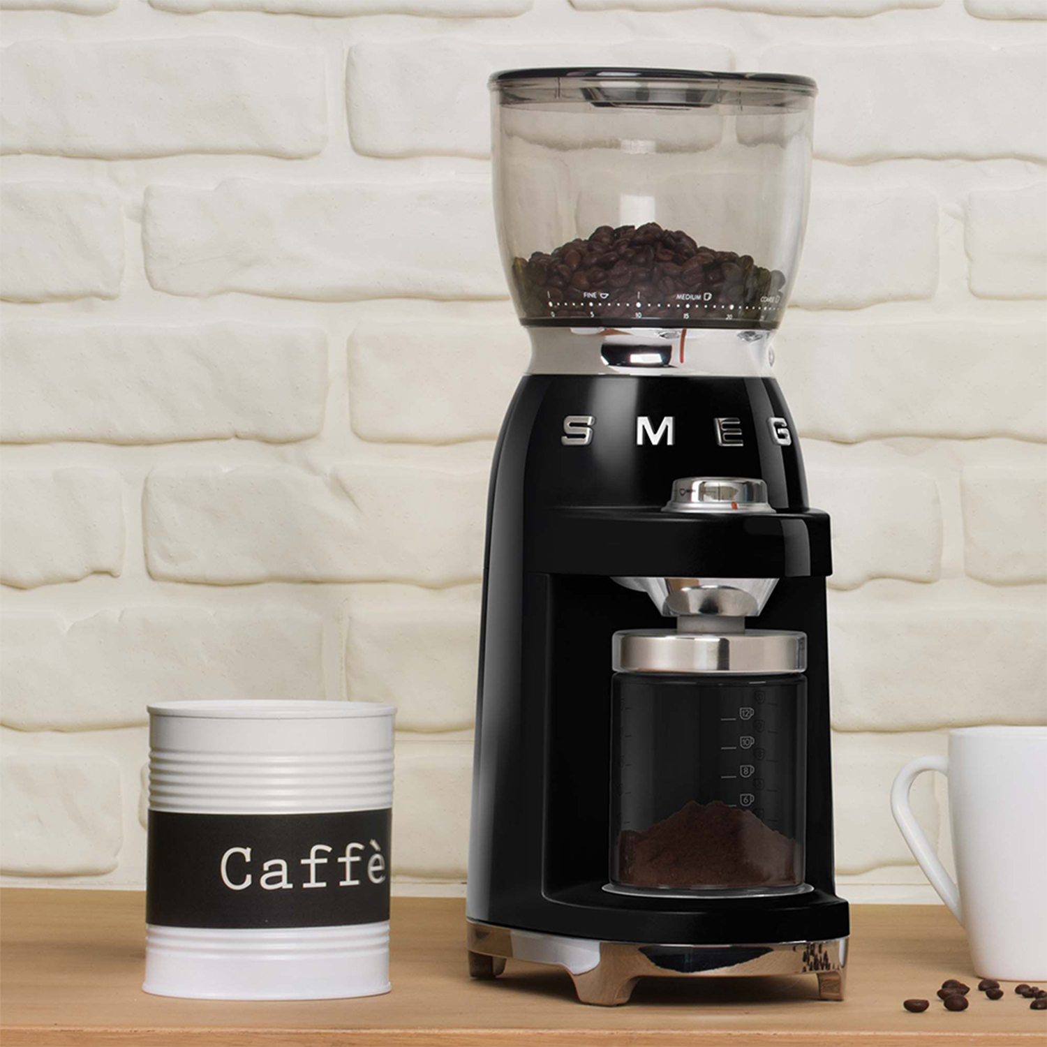 Macinacaffè nero con contenitore in vetro e barattolo bianco con 'Caffè'.
