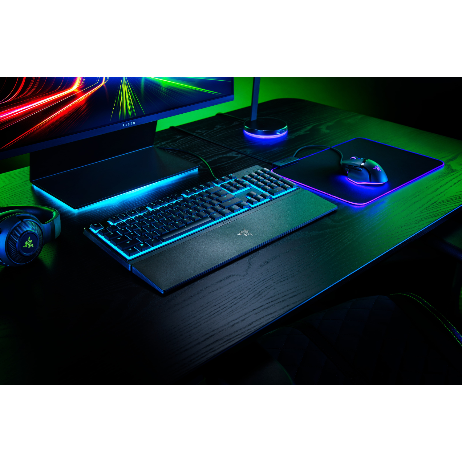 Gaming setup: toetsenbord met blauw licht, muis, monitor en koptelefoon op een zwart bureau.