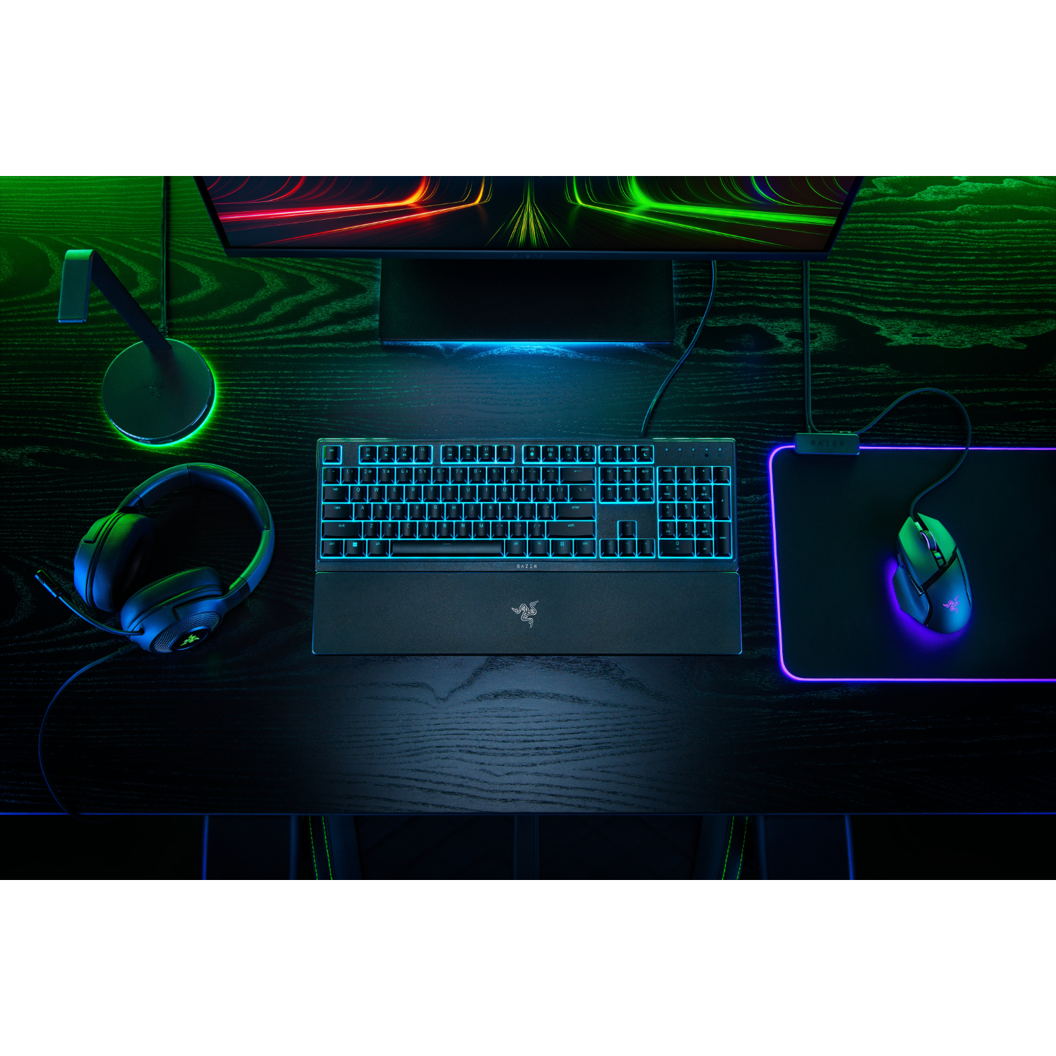 Gaming setup met toetsenbord, muis, headset en monitor, verlicht met groene en blauwe lichten.