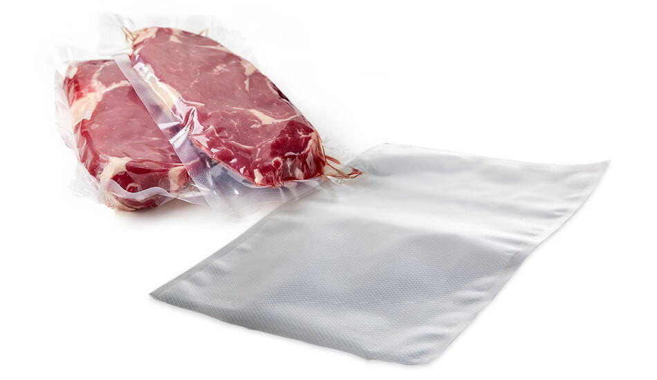 Két vákuumcsomagolt nyers steak. Egy üres vákuumcsomagoló zacskó fekszik mellettük fehér felületen.