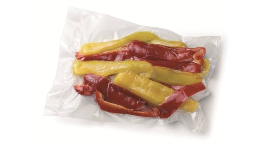 Szeletelt piros és sárga kaliforniai paprika átlátszó műanyag zacskóban fehér háttér előtt.