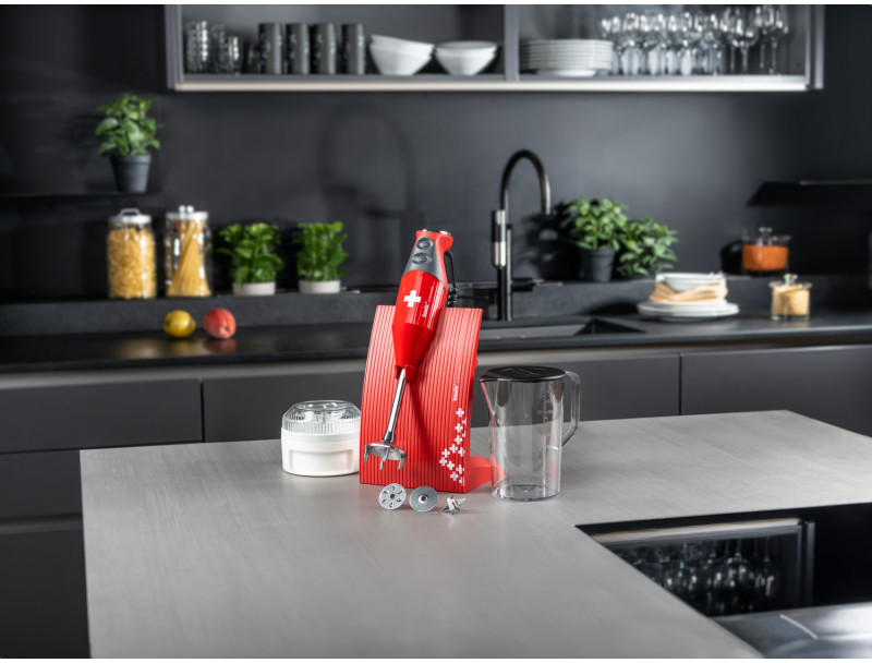 Frullatore a immersione rosso con accessori su un piano cucina.