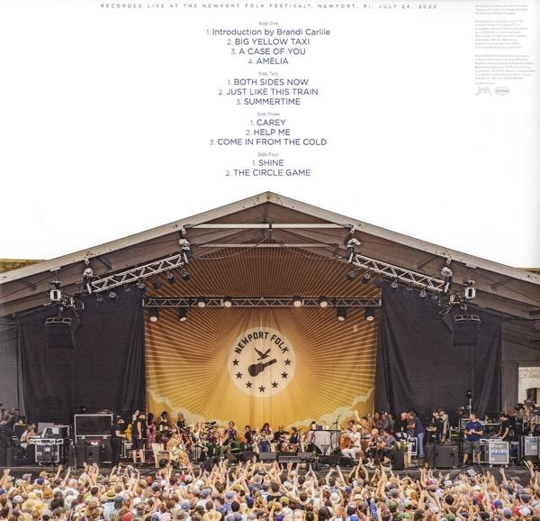 Live-Musikbühne mit spielender Band. Großes Banner mit Logo, Publikum davor.