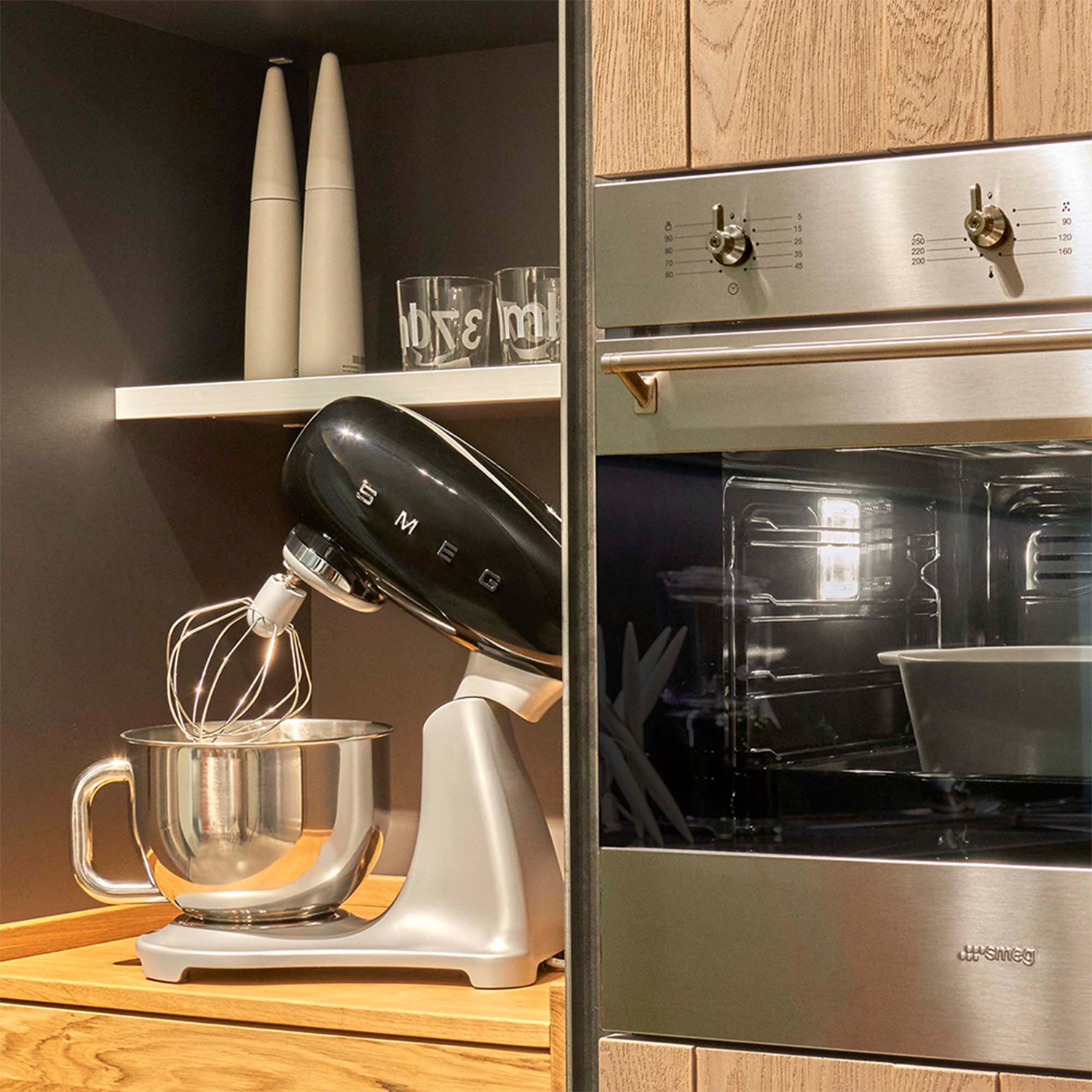 Scena cucina con planetaria nera accanto a forno, con mensole e decorazioni.