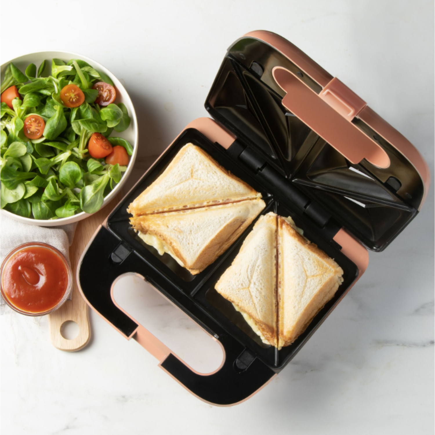 Une machine à sandwichs avec deux sandwichs, une salade et un bol de sauce.