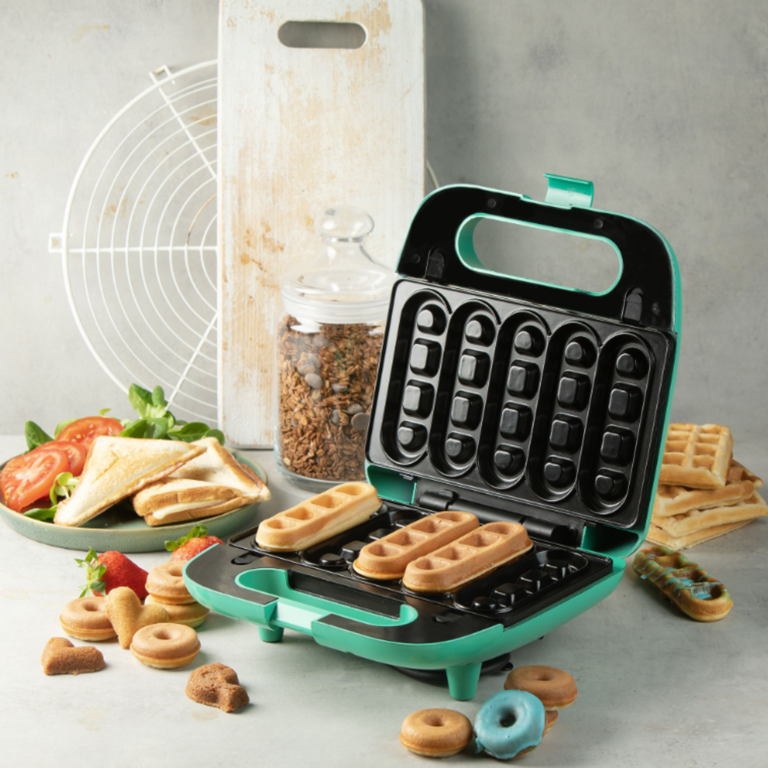 Open waffle maker with waffles, donuts, and other food items on a table. Ingredients and other items are present.