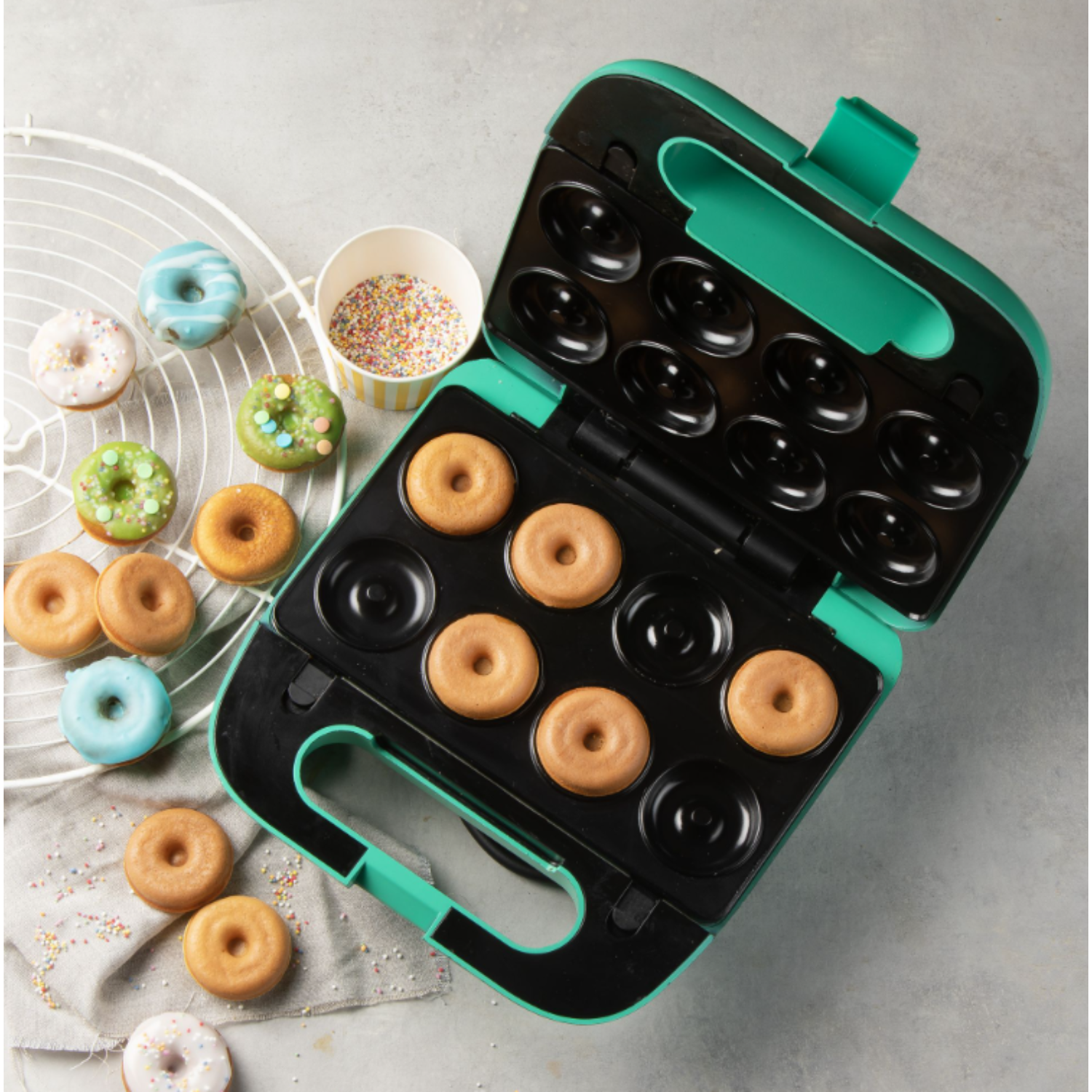 Donut maker with donuts and sprinkles. Donuts are on a white rack and in a cup, some are glazed.