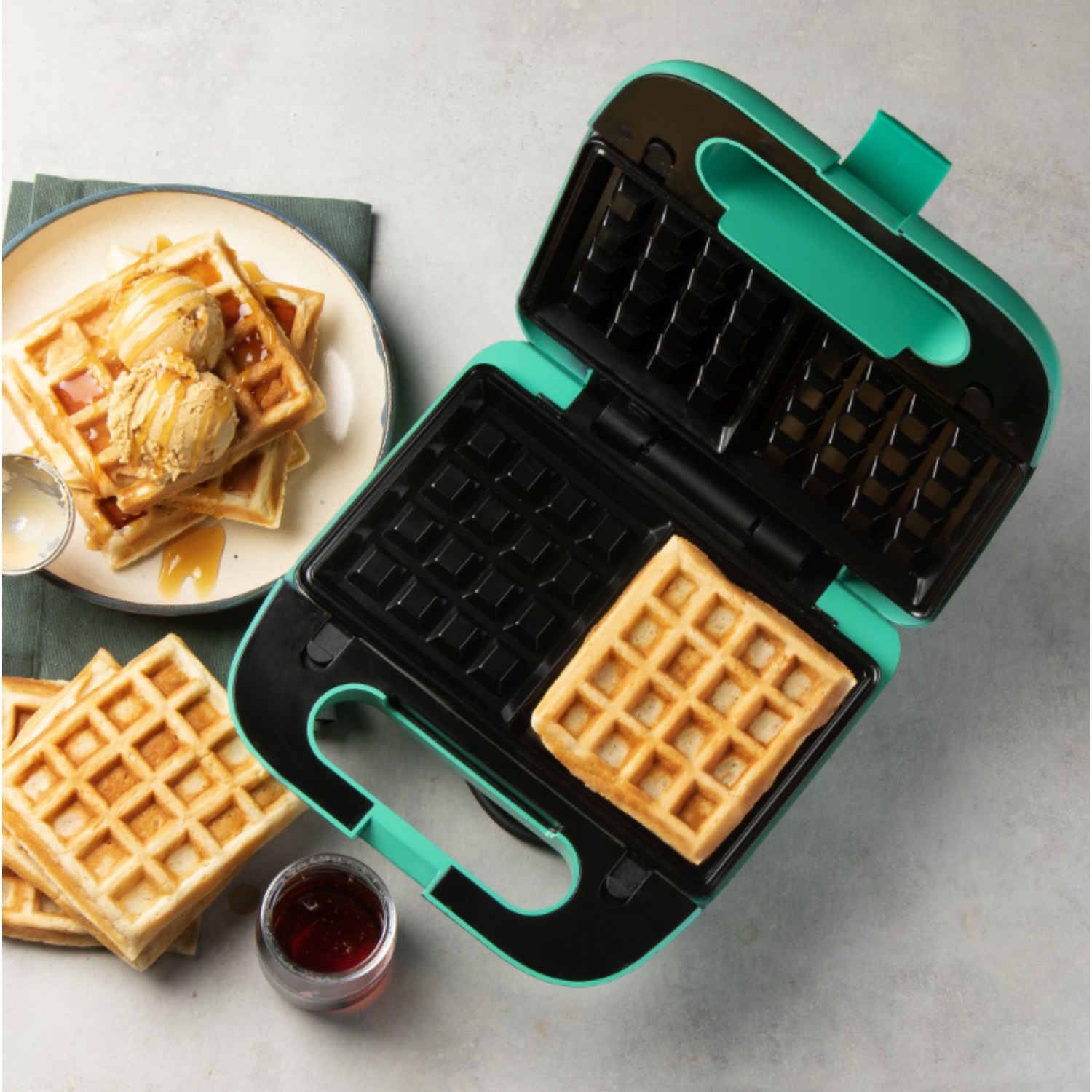 Waffle maker with a waffle inside, other waffles on the plate. Syrup and toppings.