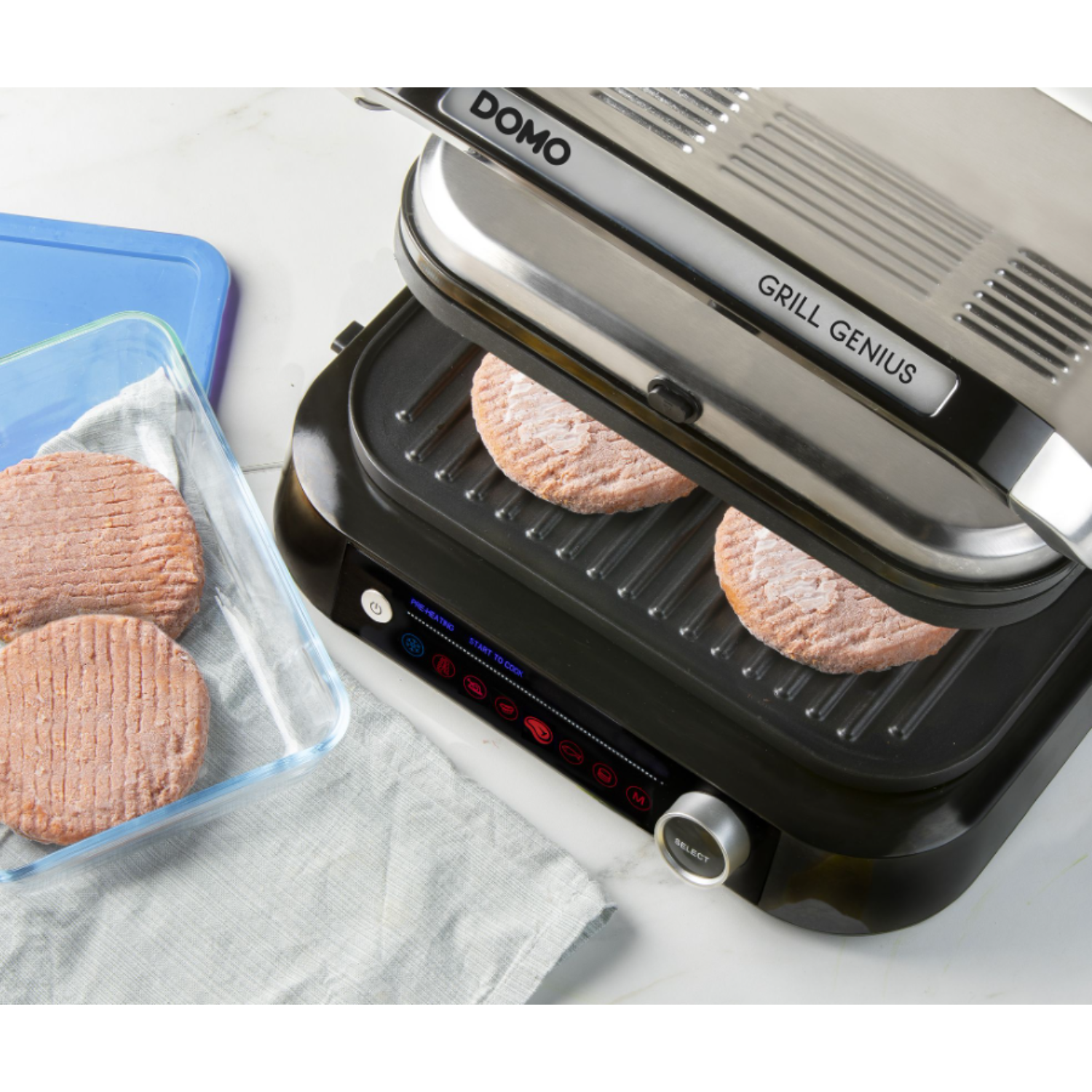 A grill with two frozen burger patties, with a blue container of patties to the side.