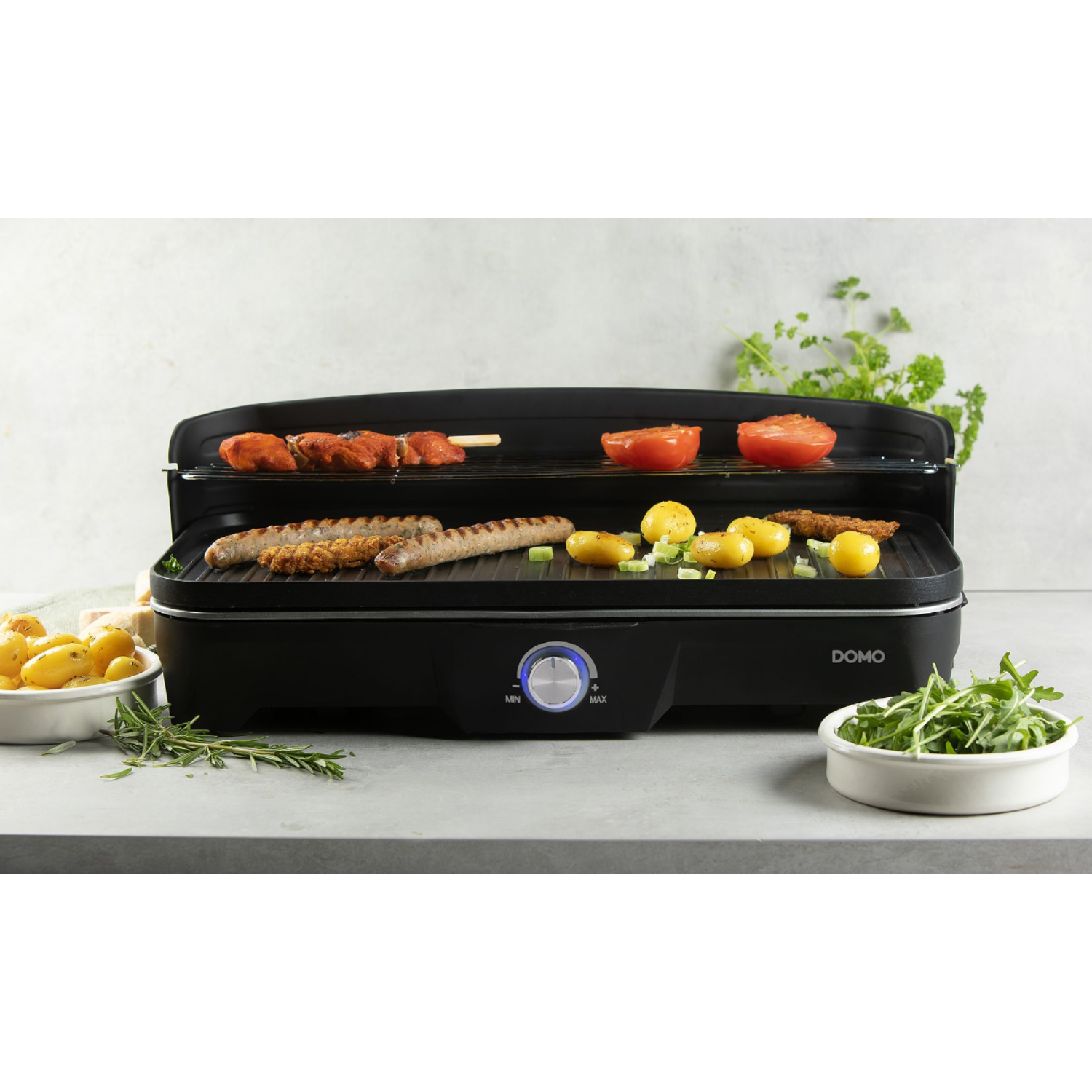 Een zwarte elektrische grill met eten erop, plus bijgerechten en een draaiknop.