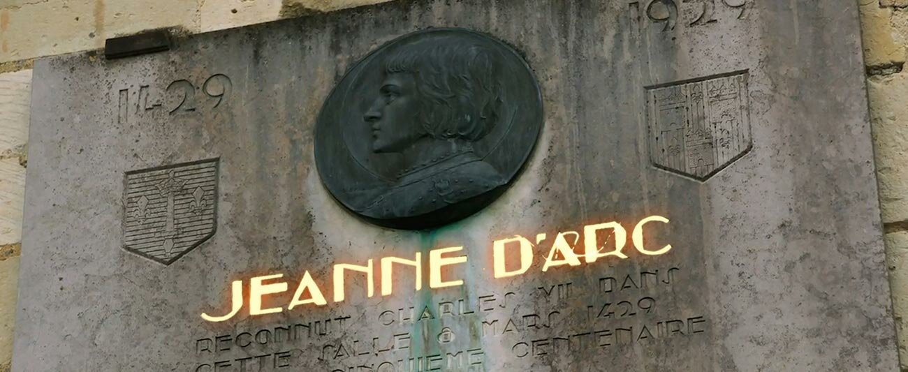 Kamienna tablica upamiętniająca Joannę d'Arc. Tekst złotymi literami i dwa herby.