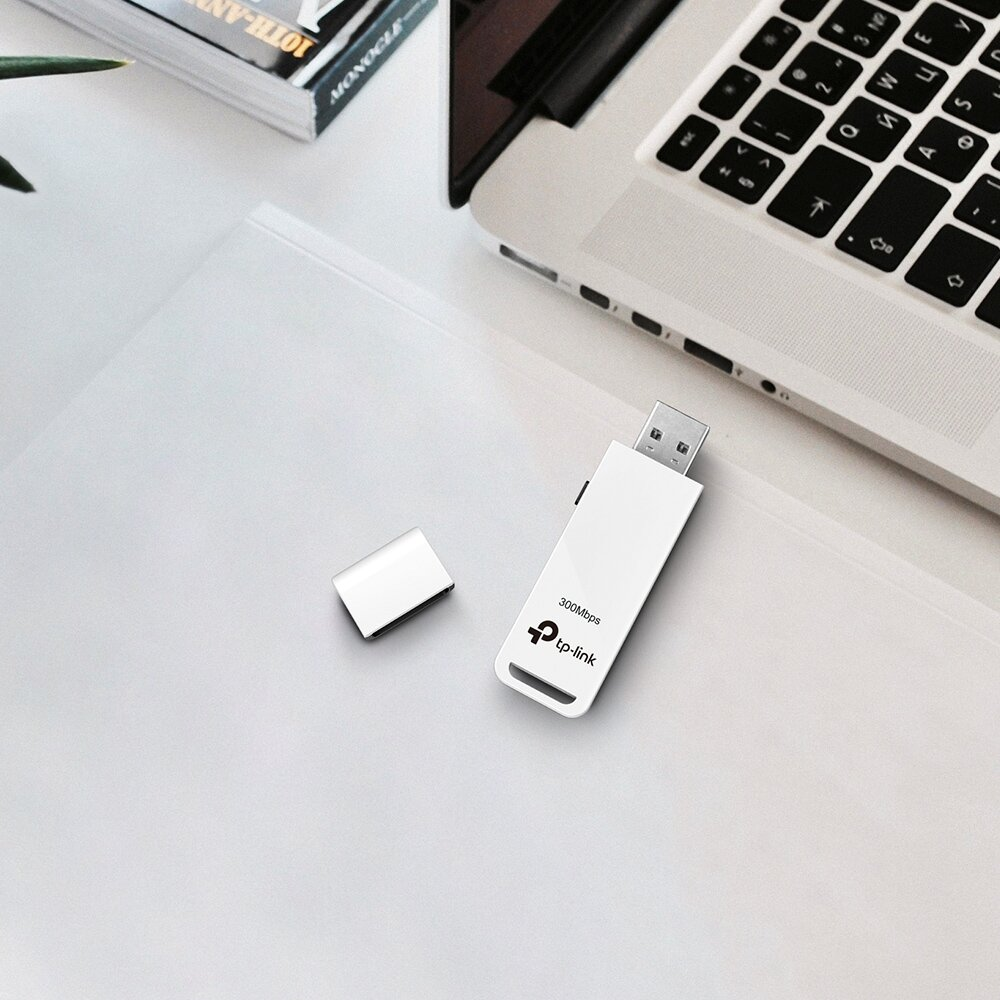 Biały adapter wifi USB i nasadka na białym biurku z laptopem.