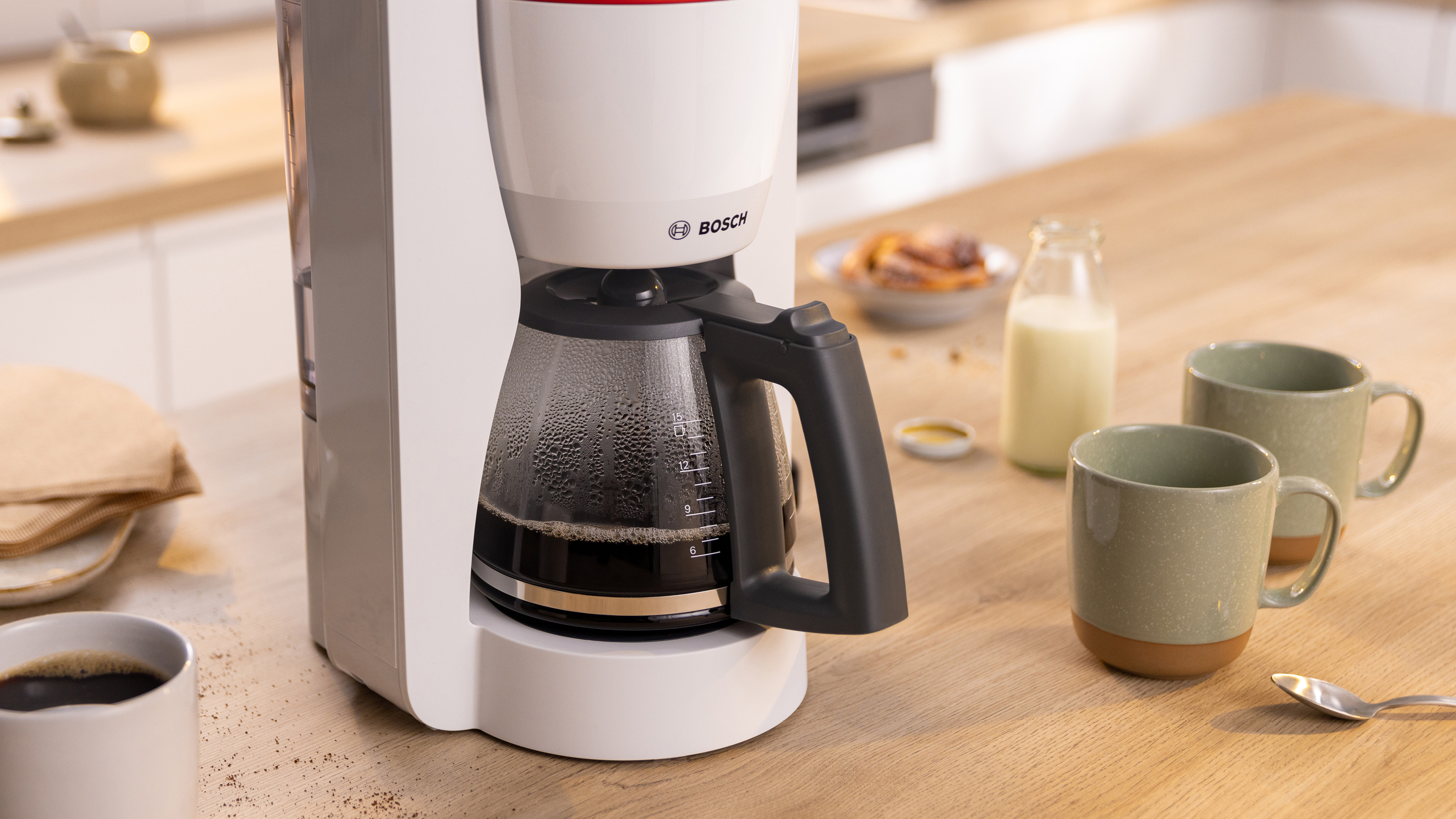 Eine weiße Kaffeemaschine mit Glaskaraffe, neben Tassen und einer Milchflasche.