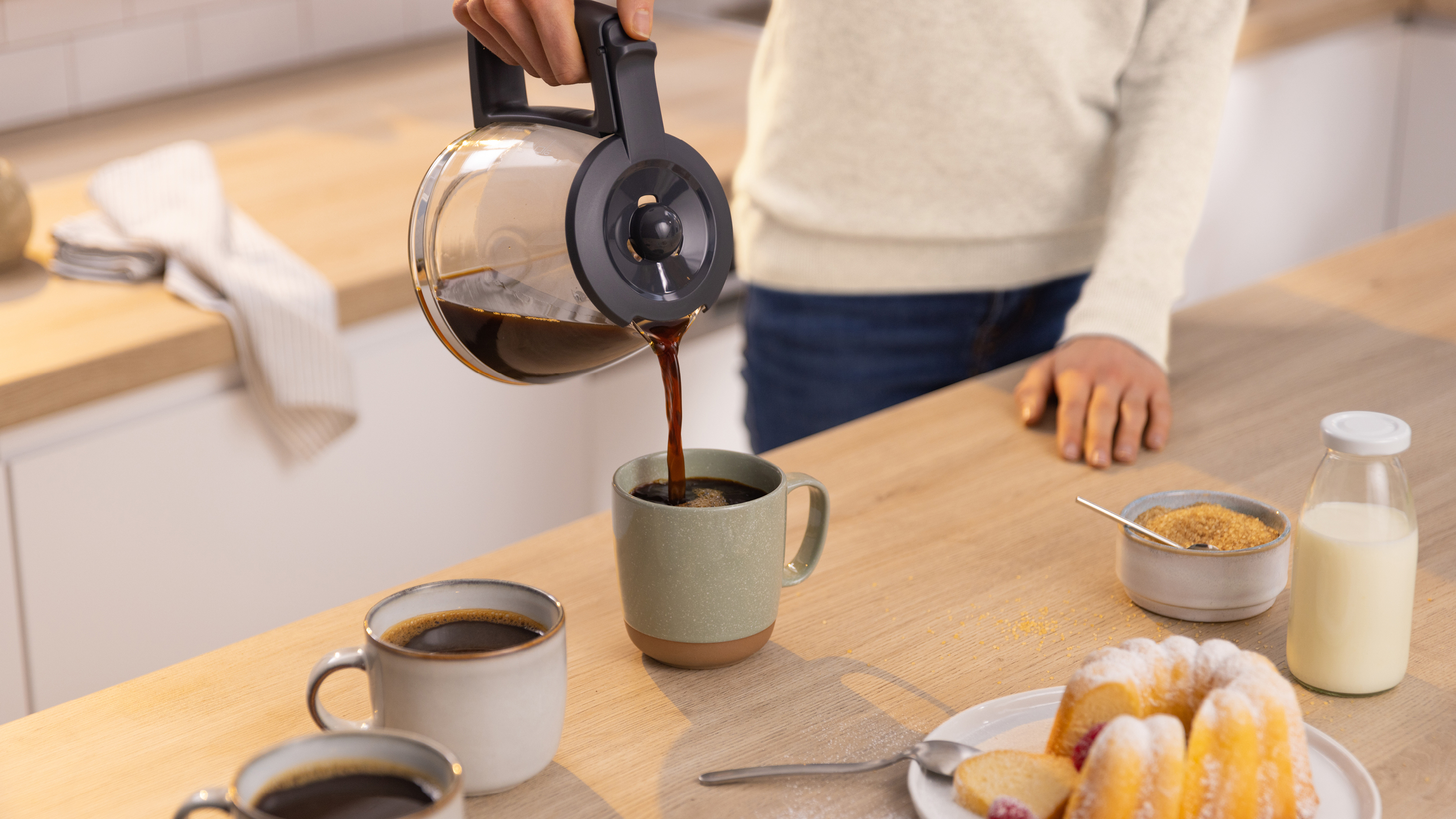 Person gießt Kaffee aus einer Glaskaraffe in eine Tasse.