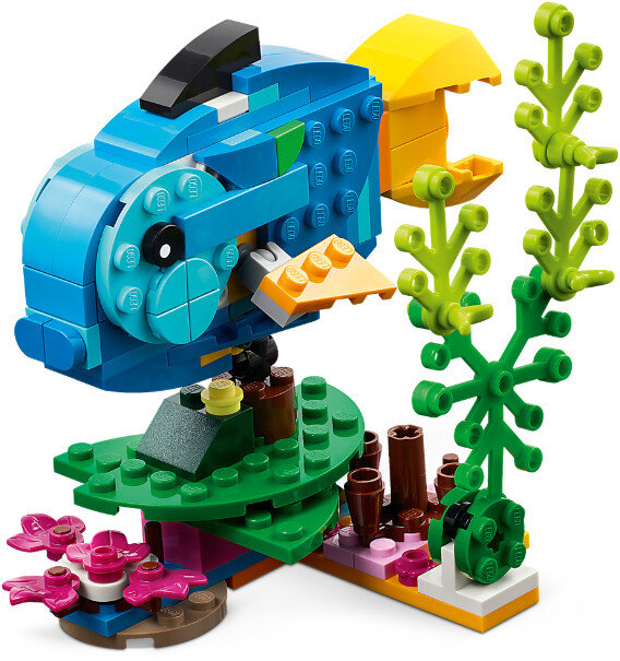 Niebieska ryba Lego z żółtymi płetwami i zielonymi koralowcami na zielonej i różowej podstawie.