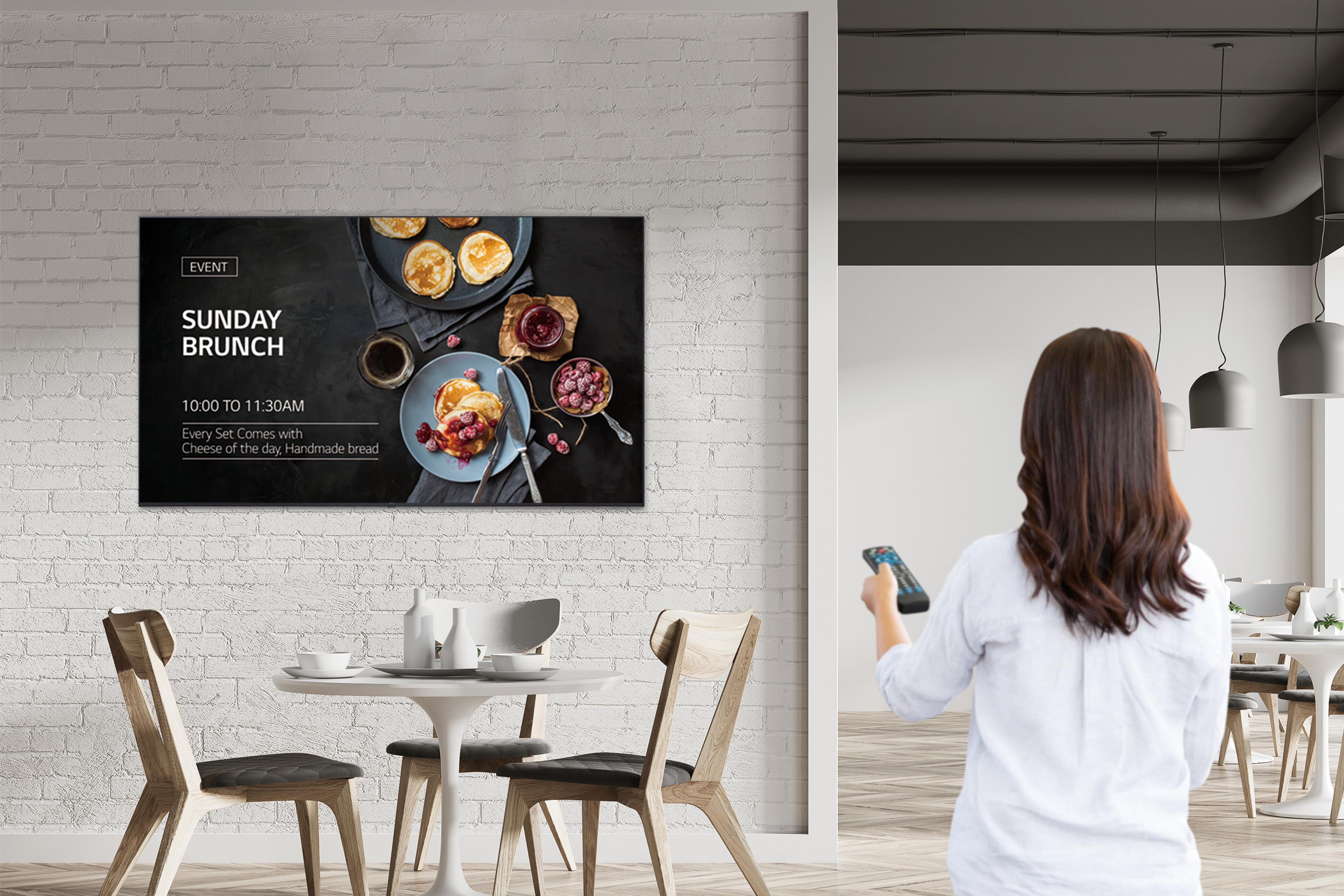 Frau hält Fernbedienung, blickt auf TV-Bildschirm mit Brunch-Menü.
